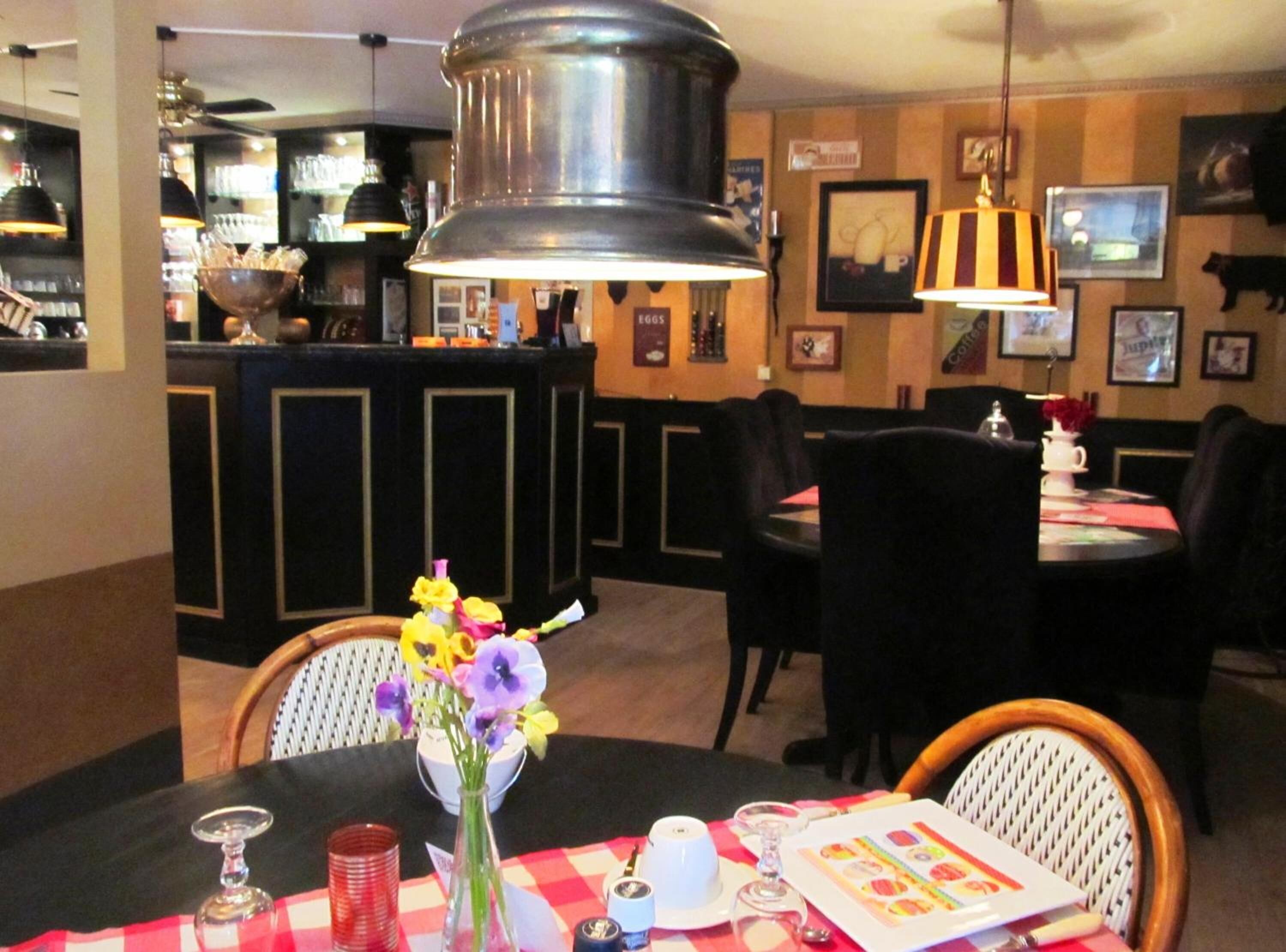 A restaurant interior with a bar area, black and white checkered tablecloths, and a vase with flowers on the table.