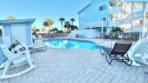 A pool area with lounge chairs, a pool, and a building with balconies.