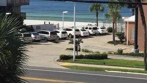 A parking lot with several white cars, a building with a balcony, and a view of the ocean.