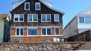 Une maison à deux étages, avec des fondations en pierre, de nombreuses fenêtres et un petit porche.