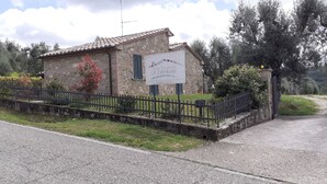 Un edificio in pietra con una targa, circondato da una recinzione in metallo nero e vegetazione.