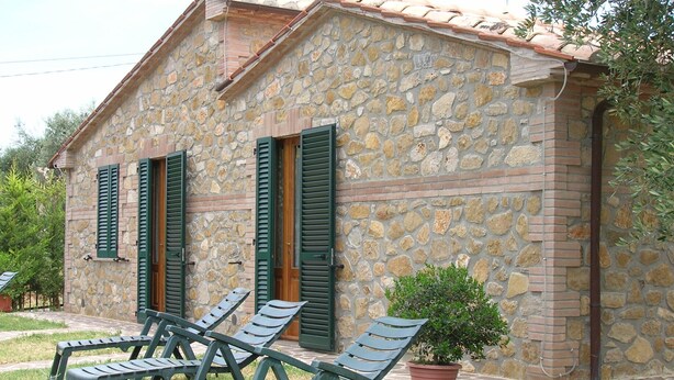 Un edificio in pietra con persiane verdi e un piccolo vaso con una pianta.