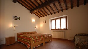 Una camera da letto con due letti, una finestra con tende, un termosifone e un soffitto in legno.