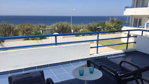 Un balcon avec deux chaises et une petite table, offrant une vue sur la côte et un ciel dégagé.