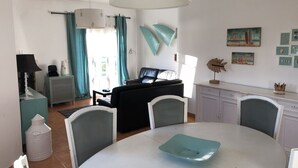 Un coin repas avec une table ronde, des chaises et un vase décoratif. On aperçoit un canapé noir et un meuble blanc à l’arrière-plan.