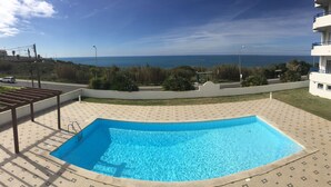 Une piscine avec vue sur la mer, entourée d’une terrasse à motifs et d’un bâtiment doté de balcons.