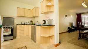 A compact kitchen with wooden cabinets, a microwave, a refrigerator, and a dishwasher. - City Airport Apartment Nairobi (Syokimau)