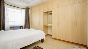 A bedroom with a bed, wooden wardrobe, a desk, and a chair. - City Airport Apartment Nairobi (Syokimau)