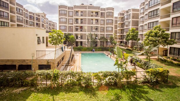 A courtyard with a swimming pool surrounded by multi-story residential buildings, stairs, and greenery. - City Airport Apartment Nairobi (Syokimau)