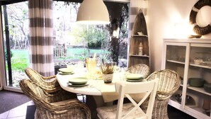 A dining area with wicker chairs, a round table, and a view of the garden through large windows. - Vacation in peace & nature - apartment on the Bodden with fenced plot. & water access (Wiek)