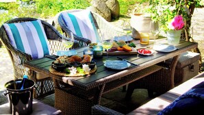 An outdoor dining area with wicker furniture, a table set with plates, glasses, and a bottle of wine. - Vacation in peace & nature - apartment on the Bodden with fenced plot. & water access (Wiek)