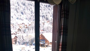 Een kamer met een raam dat uitkijkt op een besneewd berggebied, een radiator en een tafel met een boek.