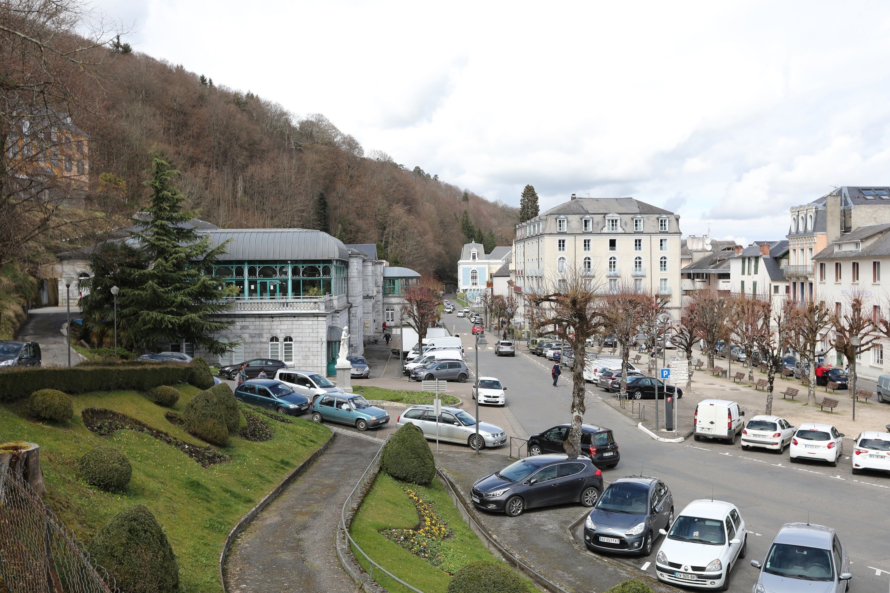 A street view with parked cars, a building with a dome, and a statue in the foreground.