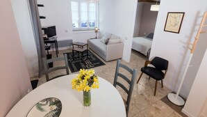 Uma sala de estar moderna com área de jantar, apresentando uma mesa redonda com um vaso de flores, um sofá e uma televisão.