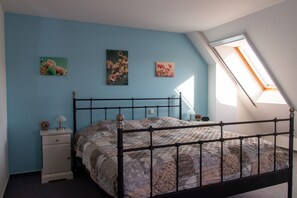 A bedroom with a bed, a nightstand, a lamp, and two wall-mounted pictures.