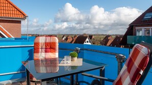 Una terraza en la azotea con una mesa, sillas y una planta en maceta.