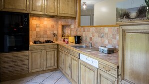 A kitchen with wooden cabinets, a black stove, and a tiled backsplash. - GITE 3 EPIS BETWEEN LAMBALLE AND PLANCOET FOR 8 PERSONS (saint denoual)
