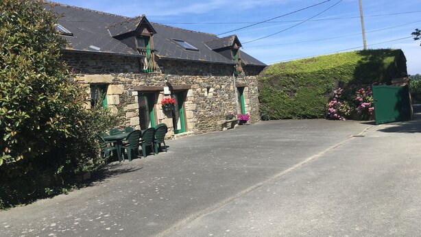 A stone building with a sloped roof, a small porch with green doors, and a paved driveway. - GITE 3 EPIS BETWEEN LAMBALLE AND PLANCOET FOR 8 PERSONS (saint denoual)