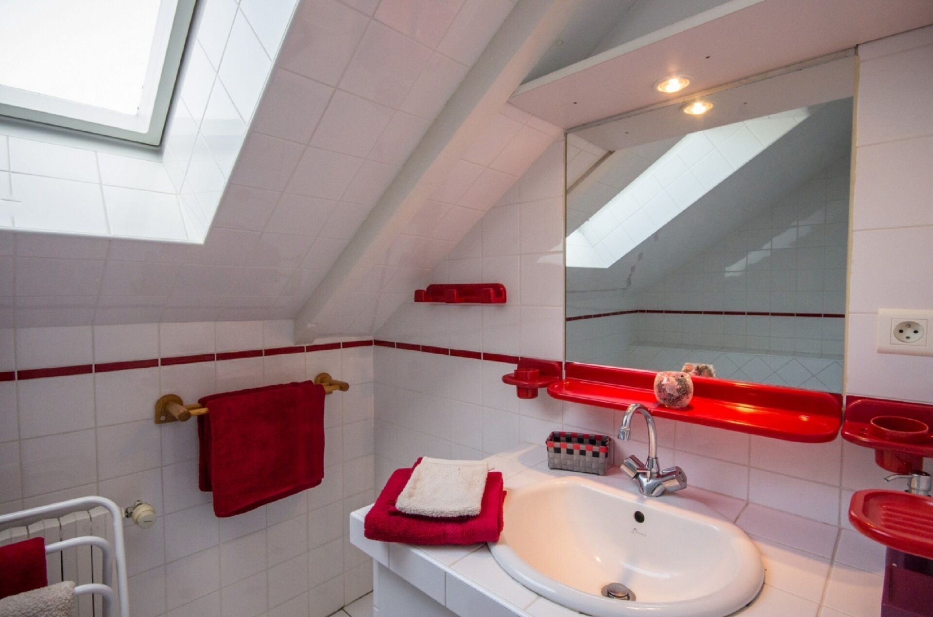 Un baño moderno con tragaluz, baldosas blancas, una toalla roja y un lavamanos blanco.