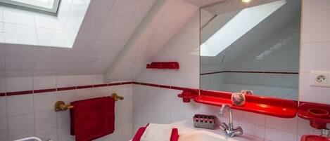 Un baño moderno con tragaluz, baldosas blancas, una toalla roja y un lavamanos blanco.