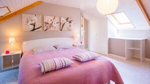 A bedroom with a sloped ceiling, a bed with pink bedding, a desk, and wall-mounted artwork. - GITE 3 EPIS BETWEEN LAMBALLE AND PLANCOET FOR 8 PERSONS (saint denoual)