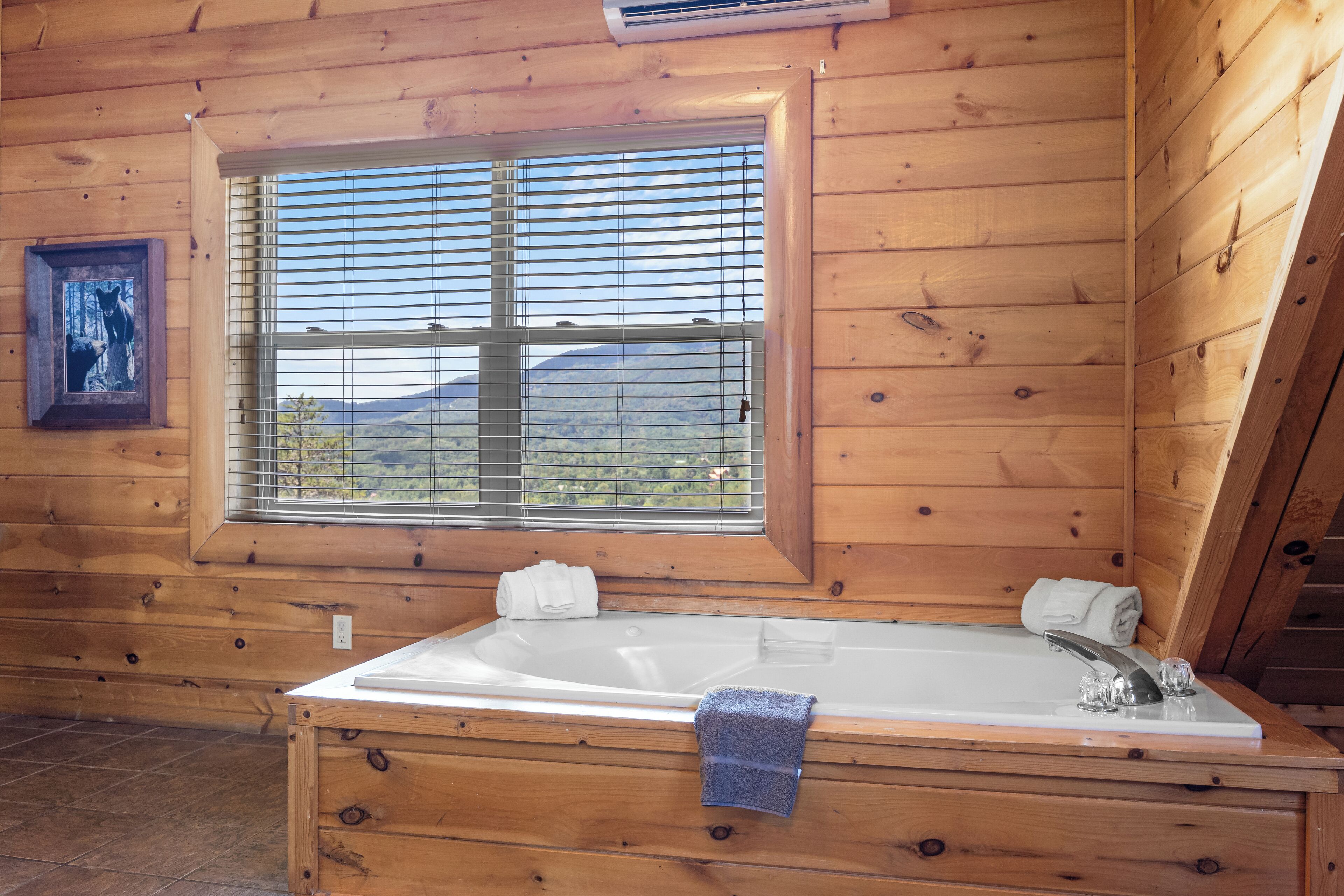 A wooden cabin with a large window, a bathtub, and a framed picture on the wall.