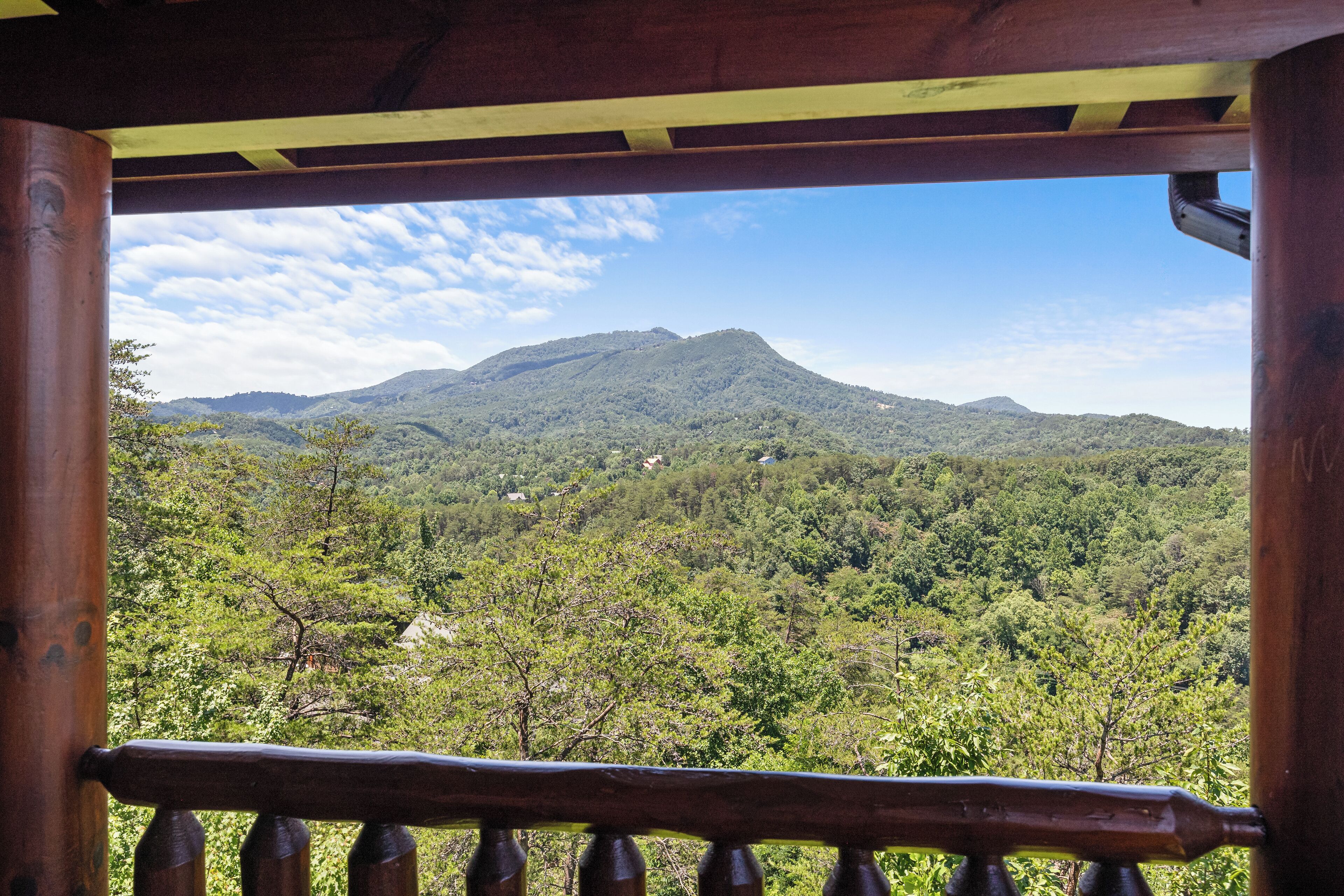 Een houten balkon met uitzicht op een bergketen en een dicht bos.