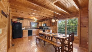 A wooden cabin interior with a kitchen, dining table, and large windows. - Mountain Views!3 miles to Pkwy,pools,putt golf,Game Room,HotTub,ColdAC topflr (Sevierville)