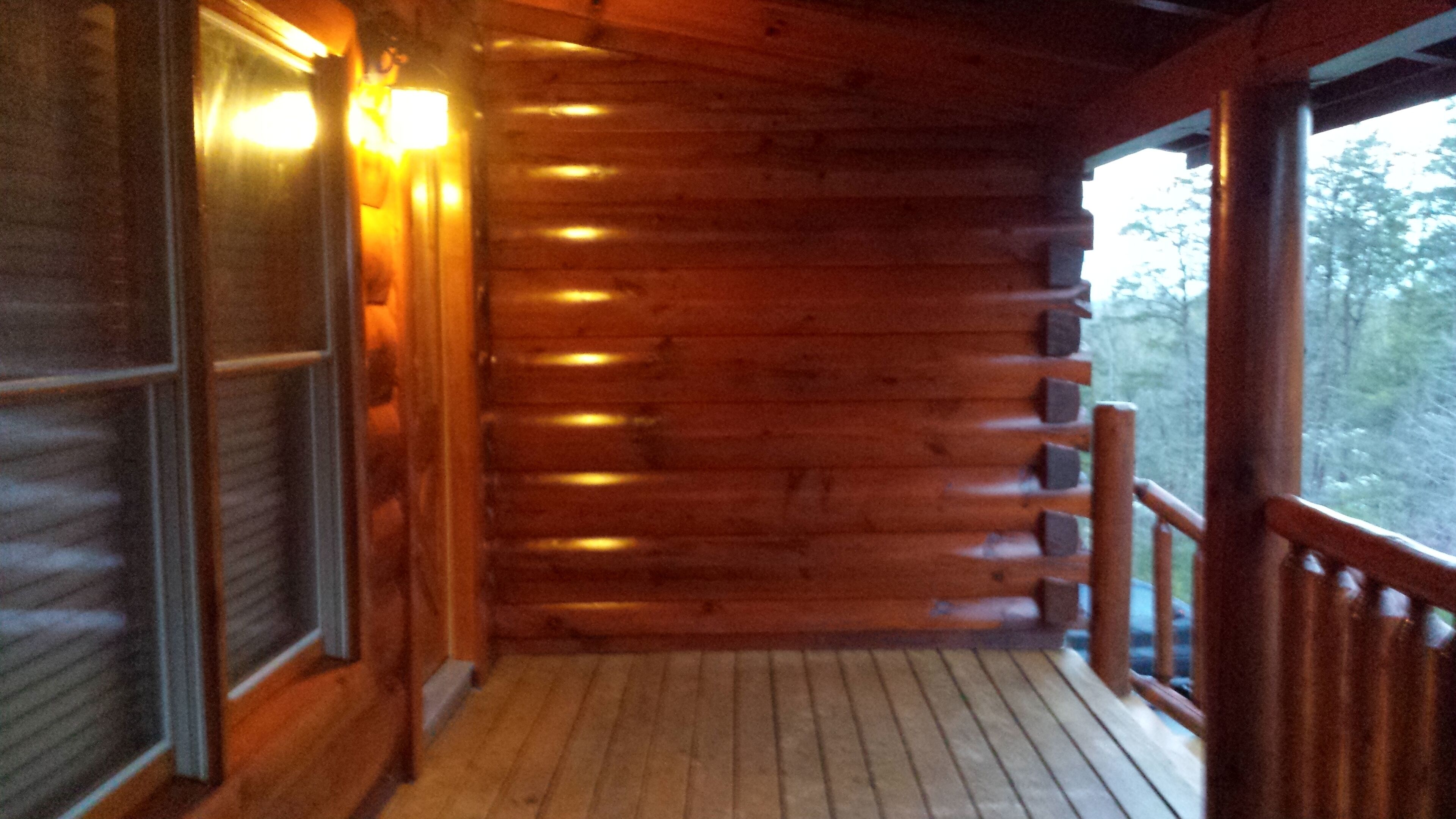 A wooden cabin with a porch, wooden walls, and a window with blinds.