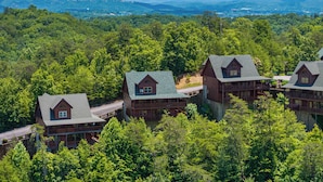 A lodge with multiple cabins, surrounded by dense forest and mountains in the background. - Mountain Views!3 miles to Pkwy,pools,putt golf,Game Room,HotTub,ColdAC topflr (Sevierville)