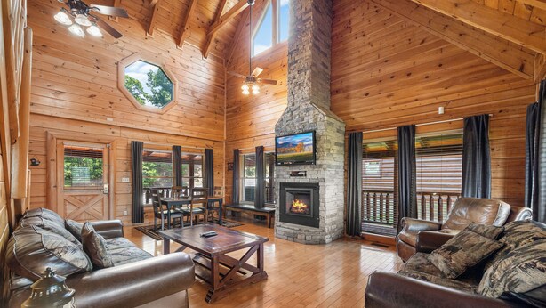 A spacious living room with wooden floors, leather sofas, a stone fireplace, and a television. - Mountain Views!3 miles to Pkwy,pools,putt golf,Game Room,HotTub,ColdAC topflr (Sevierville)