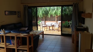 Un soggiorno con divano, tavolino e scaffali. Una porta scorrevole in vetro dà accesso a un patio esterno con tavolo e sedie.