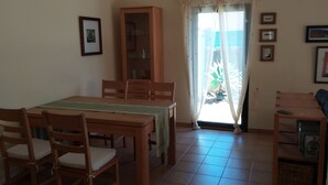 Zona pranzo con tavolo e sedie in legno, un armadio e vista attraverso una finestra con tende.