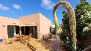 Un’area patio con pavimento in pietra, arredi in legno e un arco decorativo con piante.