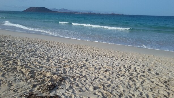 Una spiaggia sabbiosa con onde calme e una catena montuosa in lontananza.