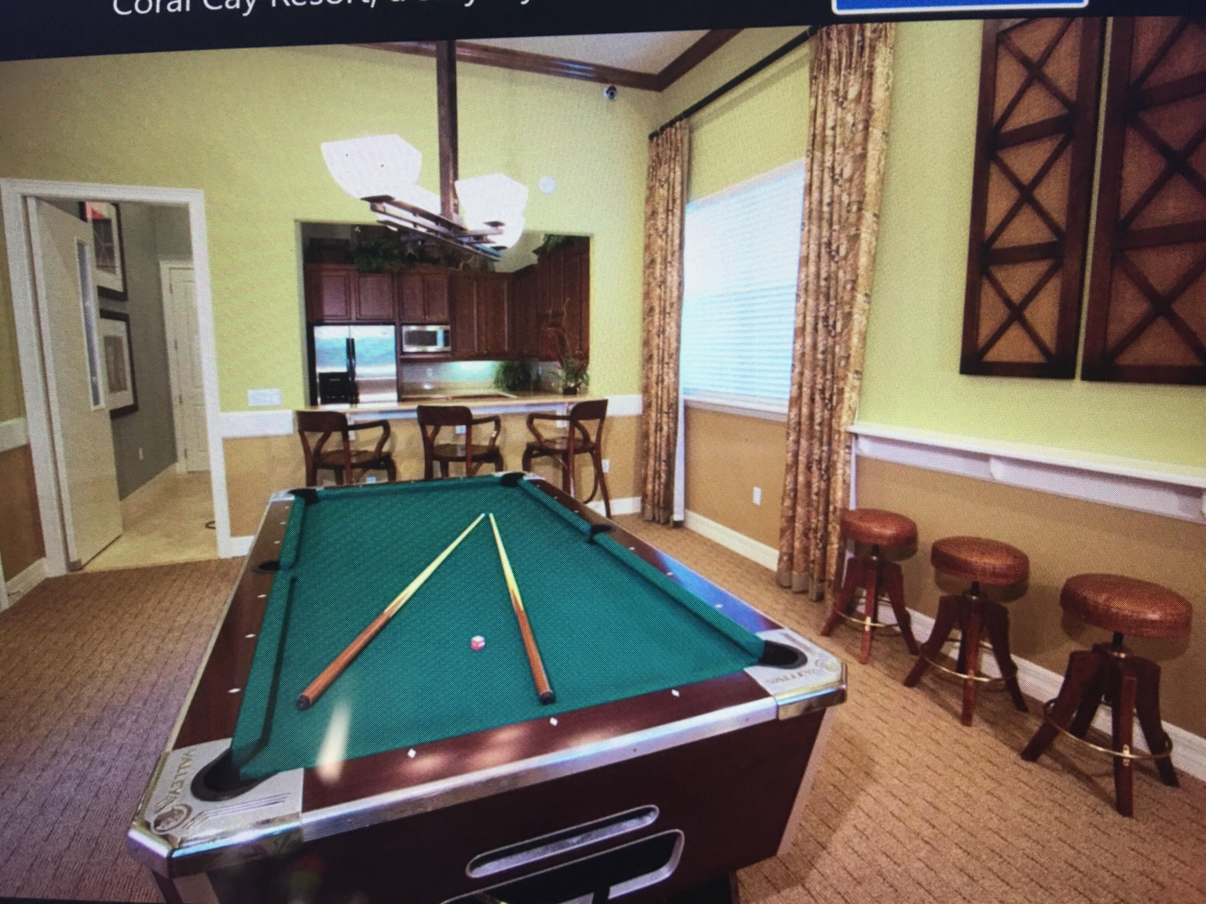A pool table in a room with a kitchen area visible through an open door.