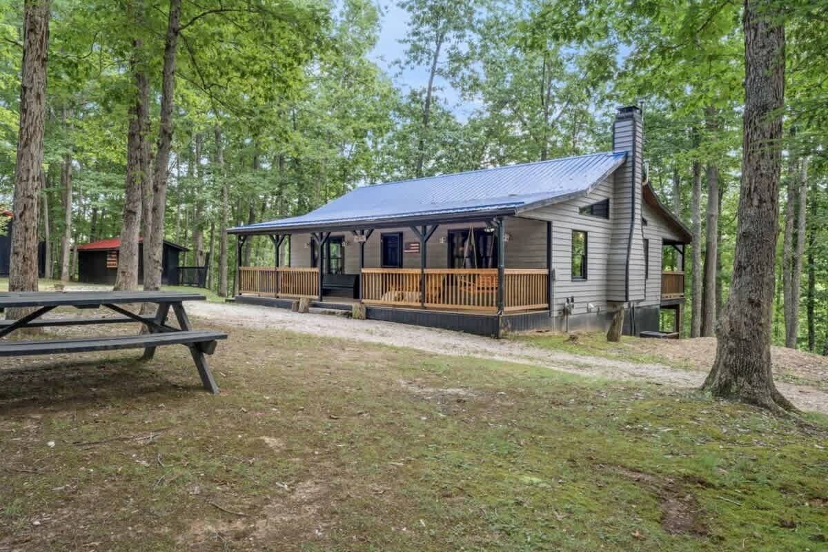 A cabin with a porch, a picnic table, and a chimney.