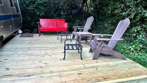 A wooden deck with outdoor furniture including a red bench and Adirondack chairs.