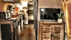 A compact kitchen with a microwave, toaster, sink, and a large flat-screen TV on a wooden cabinet.