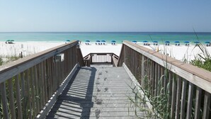 Pasarela de madera que conduce a una playa con sombrillas azules y arena blanca.