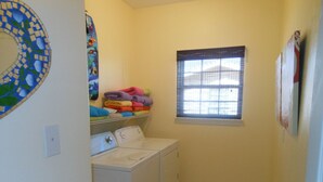 A laundry room with a washing machine, dryer, and a shelf with folded towels. - beachouse 1/2block to convention center/ restaurants/bars (Galveston)