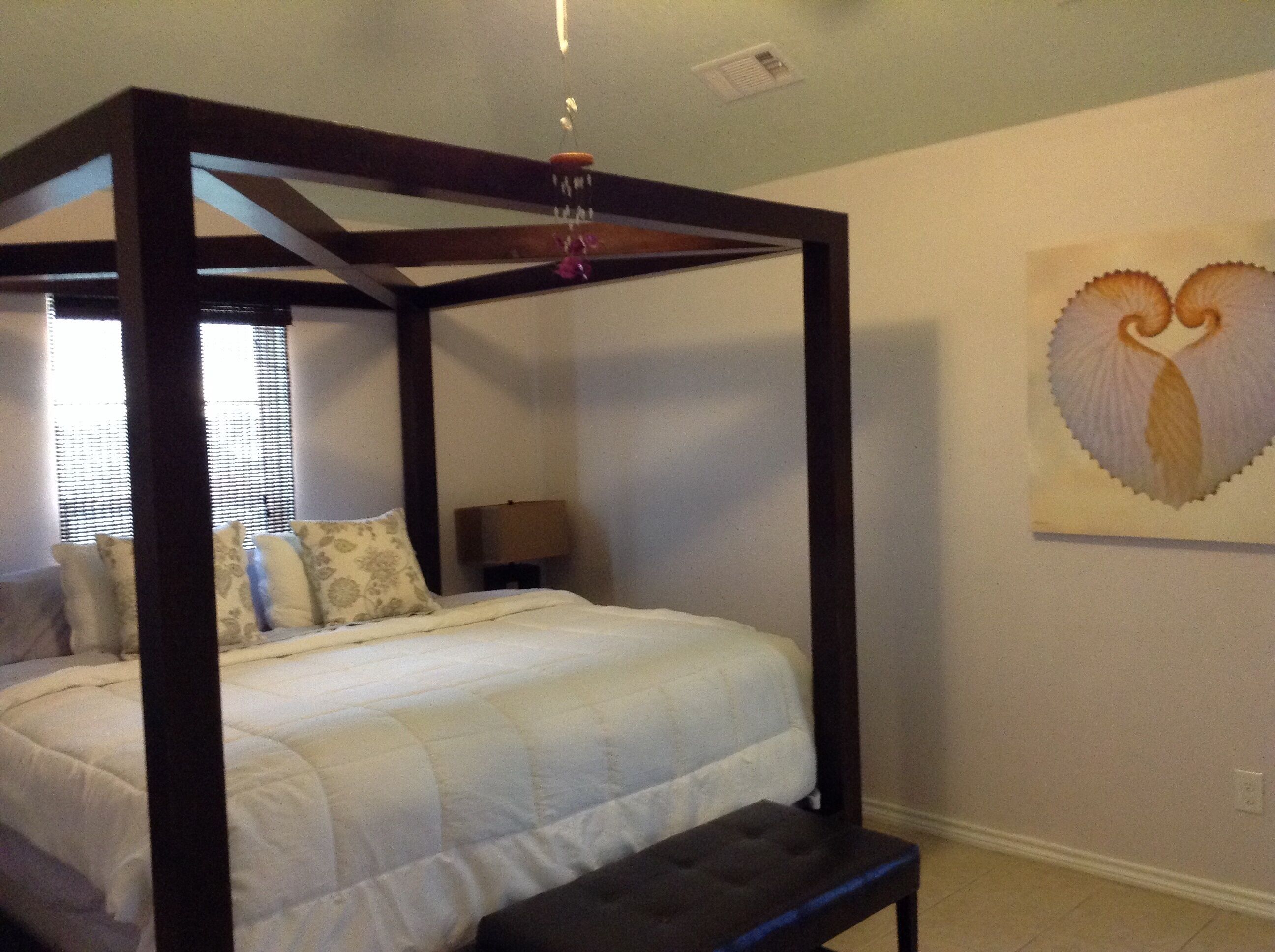 Una cama con dosel, con cubrecama y almohadas blancas, una mesita de noche con lámpara y una decoración de corazón en la pared.