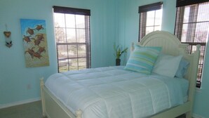 A bedroom with a bed, two windows with blinds, a wall-mounted painting, and a small plant. - beachouse 1/2block to convention center/ restaurants/bars (Galveston)