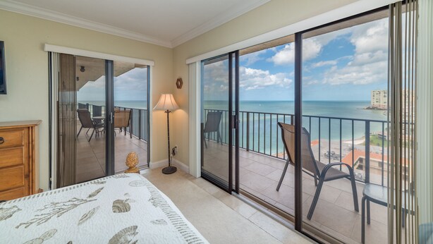A hotel room with a balcony overlooking the sea, a bed, a lamp, and a view of the ocean and buildings. - Amazing Gulf Views w/Private Beach, shelling & fishing on property! (Marco Island)