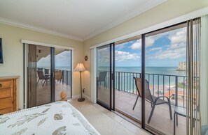A hotel room with a balcony overlooking the sea, a bed, a lamp, and a view of the ocean and buildings.