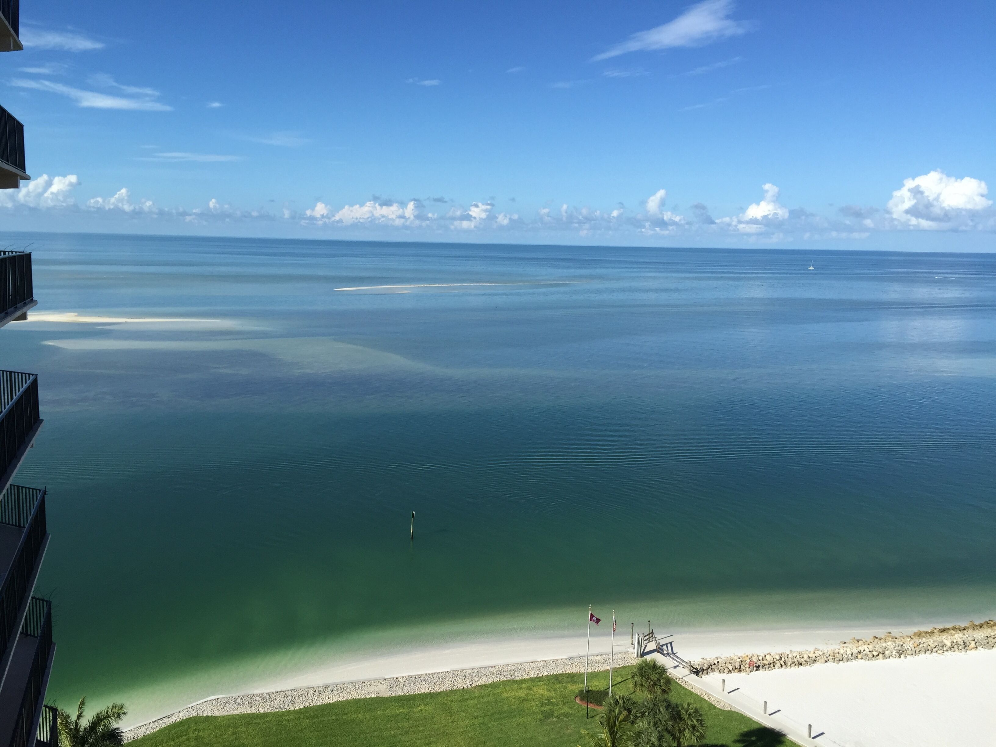 En vy över en strand med klart vatten, en sandstrand och en flaggstång med flaggor.