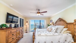 A bedroom with a bed, a television, a dresser, and a view of a cityscape through a balcony. - Amazing Gulf Views w/Private Beach, shelling & fishing on property! (Marco Island)