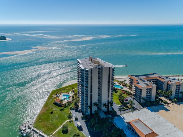 A high-rise hotel with a pool and beach access, overlooking a coastal area with clear blue waters.
