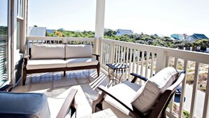 A covered outdoor seating area with a sofa and chairs, a small table, and a railing. - *PRIVATE BEACH*    *PRIVATE POOL*    *ELEVATOR*    *6 BEACH BIKES* (inlet beach)