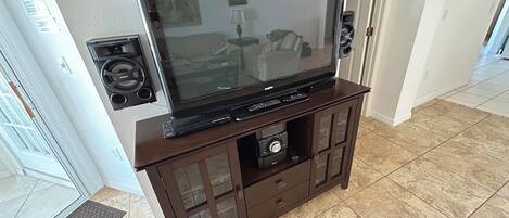 A living room with a large flat-screen TV on a wooden entertainment center, a fireplace, and a door leading to another room.